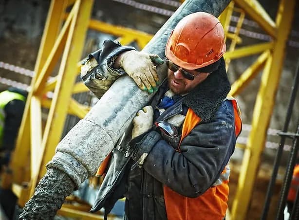 Construction worker in hard hat and hi-vis vest carrying materials on site